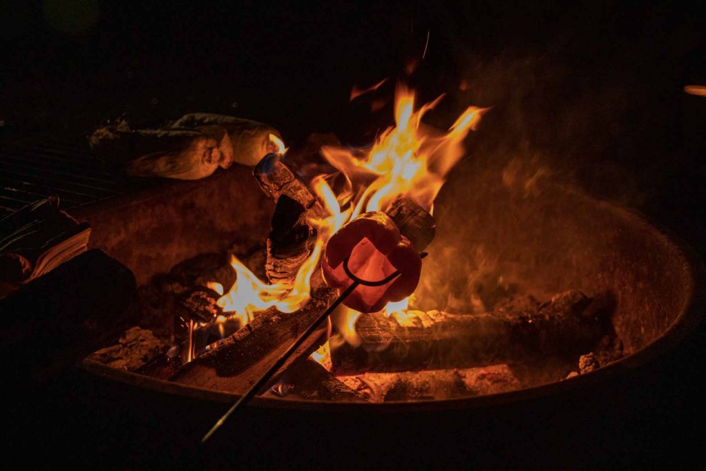 Someone roasts a pepper above a campfire.