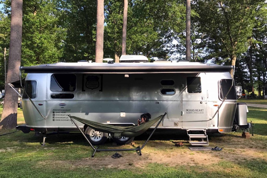 A woman sits in an ENO hammock in front of an Airstream trailer.