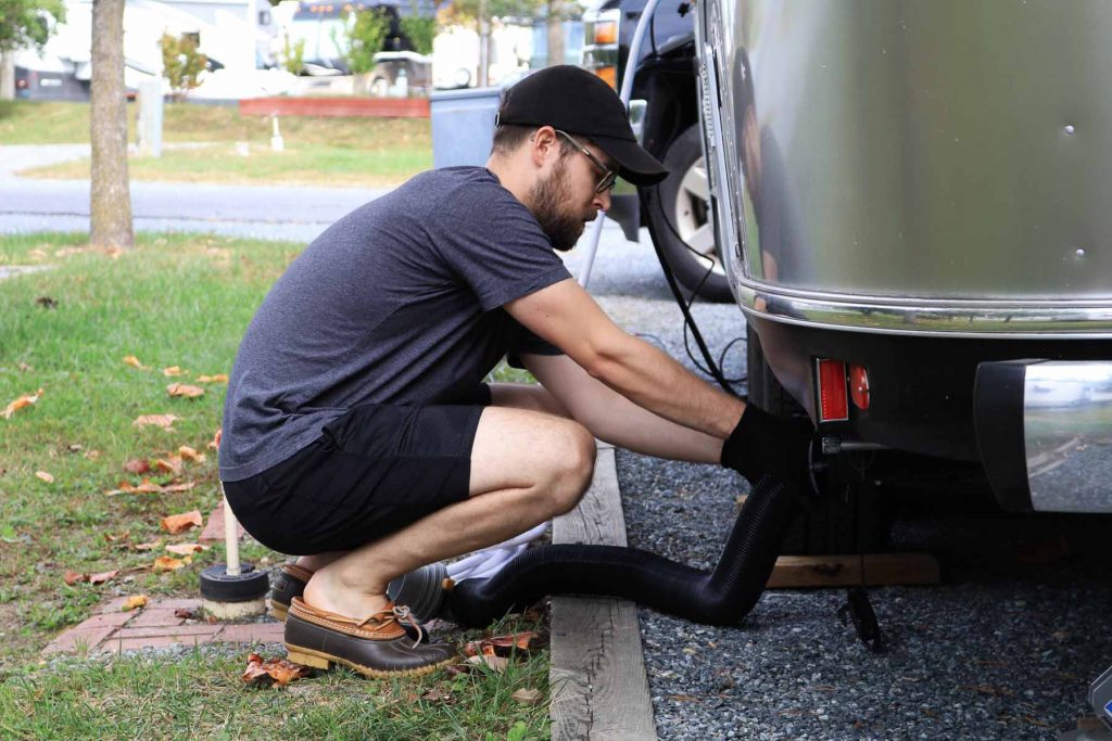 A man connects his sewage hose to his Airstream trailer.