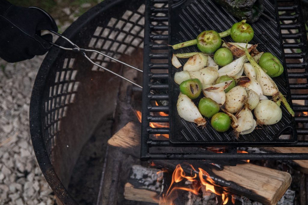 Onions and tomatillos cooking on top of a Lodge cast iron skillet over a campfire.