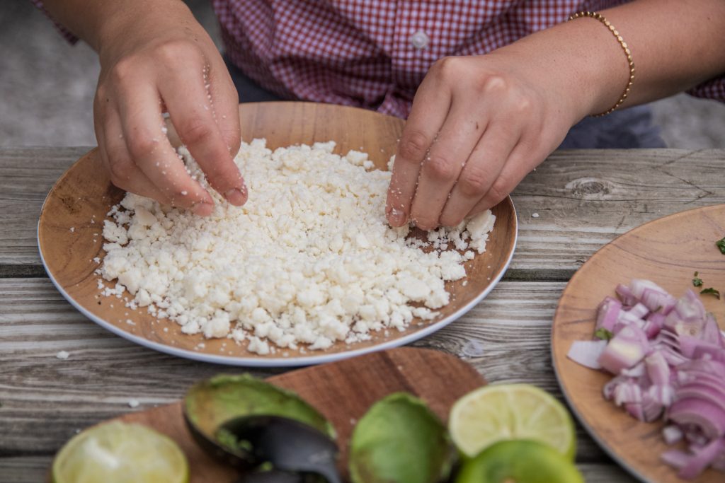 A woman crumbles cotija cheese to go on top of the nachos.