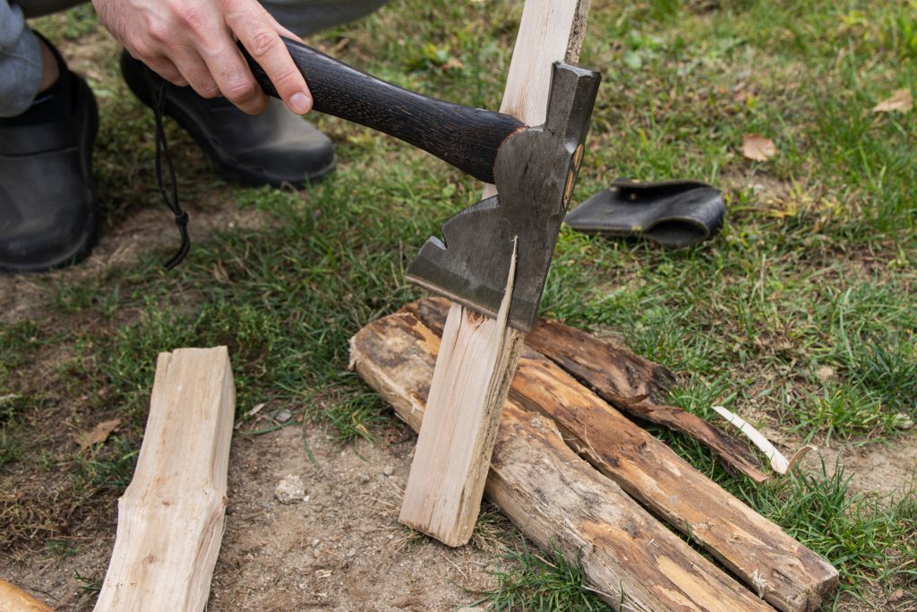 A man using a hatchet to splinter off pieces of tinder to help build a campfire.