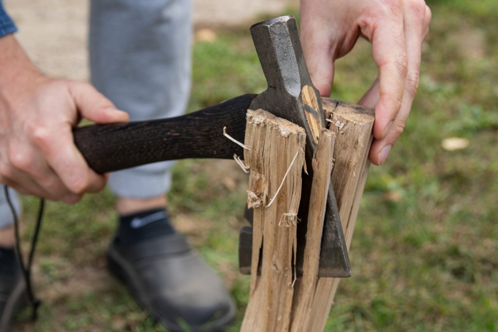 A man uses a hatchet to splinter off pieces of kindling to build a campfire.