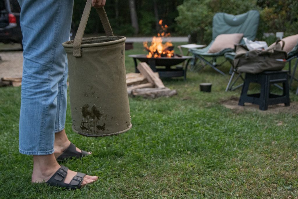 A woman holds a bucket of water to put out a campfire.