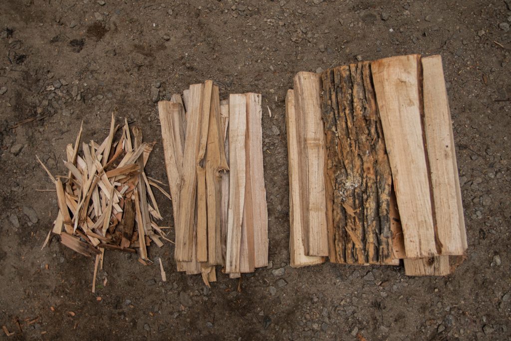 Tinder, kindling, and campfire wood piled on the ground in sequence.