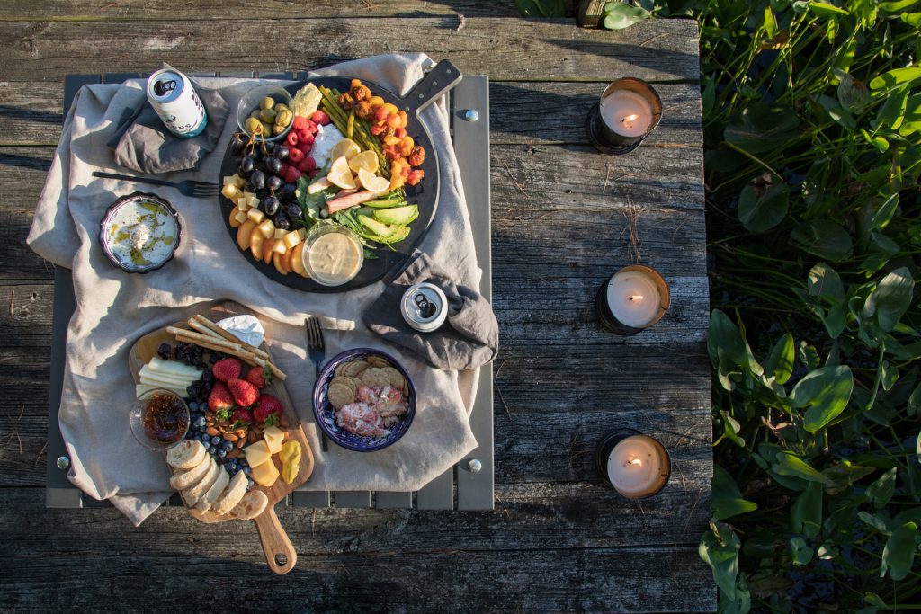 A top-down image of Crate & Barrel's Table In A bag with platters of cheese and charcuterie atop it. It seems on top of a dock with lily pads surrounding it.