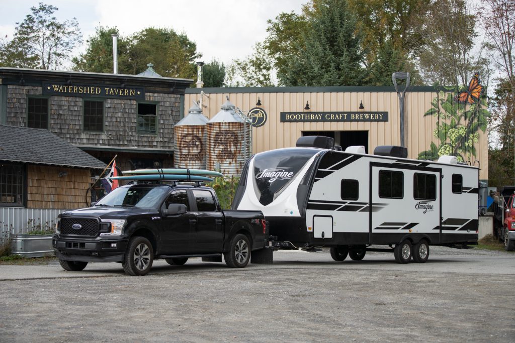 A truck with paddle boards pulling a travel trailer sits in front of Boothbay Craft Brewery in Boothbay, Maine.