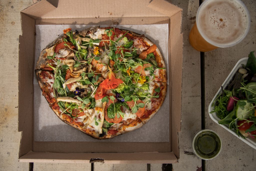 A colorful pizza and beer on top of a picnic table at Boothbay Craft Brewery in Boothbay, Maine.