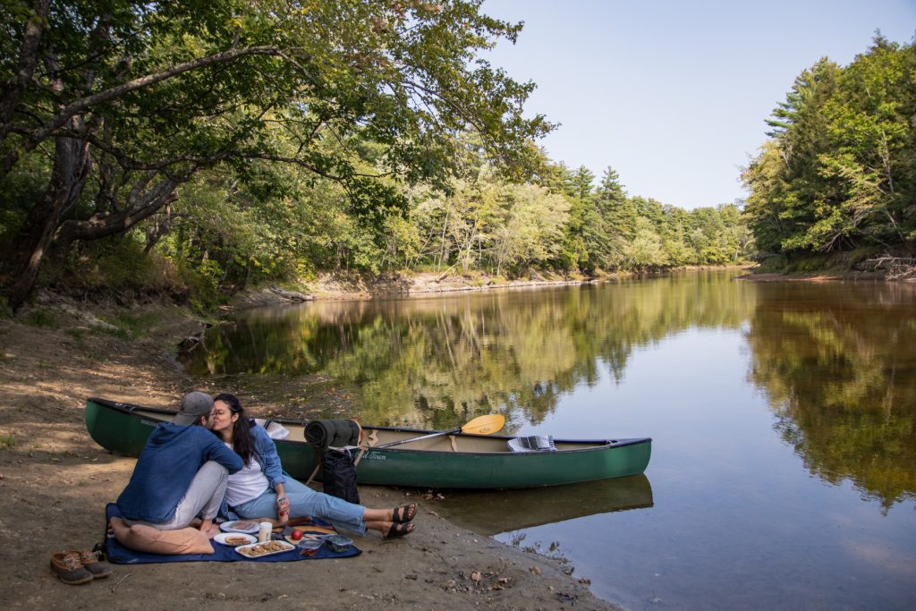 A couple kisses while taking a break from canoeing and on a picnic along the Saco river at On The Saco Family Campground in Brownfield, Maine.