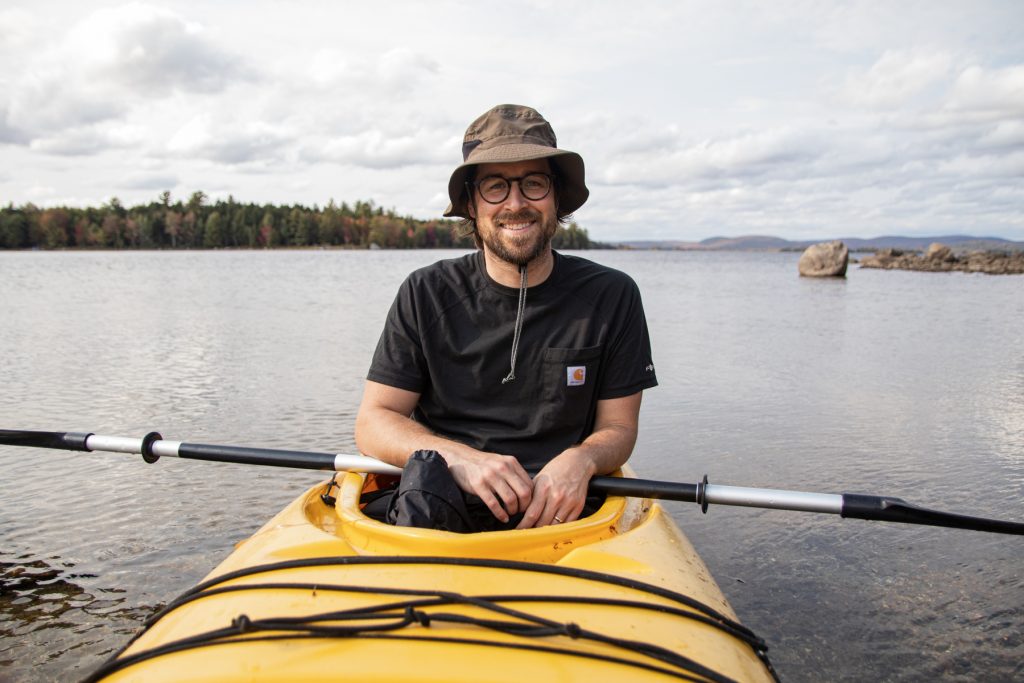 A man kayaks Junior Lake in Springfield, Maine while staying at Wild Fox Cabins and Campground.