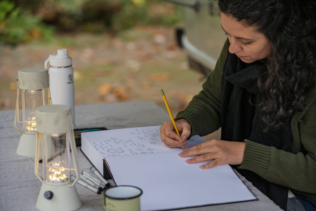 A woman sits at a campground picnic table while writing in her journal.