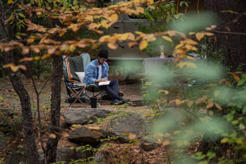 A man writes in his journal while sitting on a camp chair at his campsite.