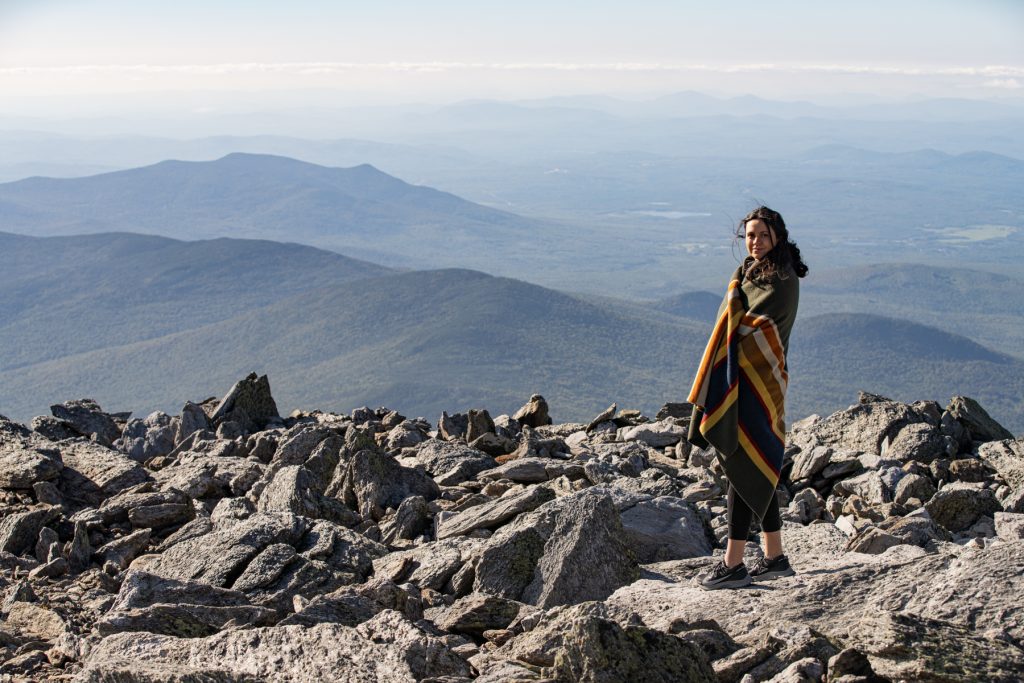 A woman wraps herself in a Pendleton blanket and looks over the Appalachian mountains on top of Mount Washington in New Hampshire.