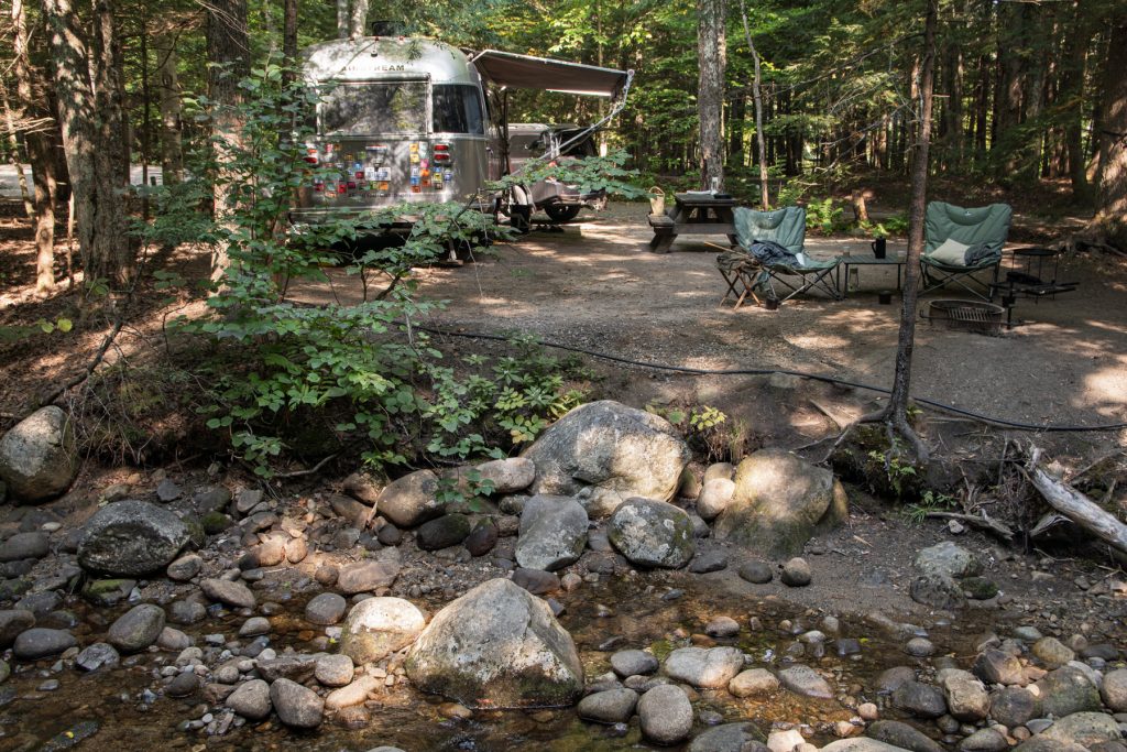 An Airstream trailer at Lost River Valley Campground in the White Mountain National Forest in North Woodstock, New Hampshire overlooking a stoney brook.