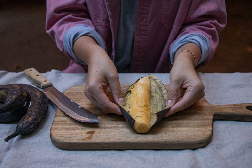 A person peels back the peel of a plantain to reveal the inside.