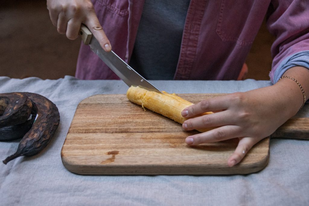 With the peel removed, a person slices the inside of a plantain in half, length-wise.