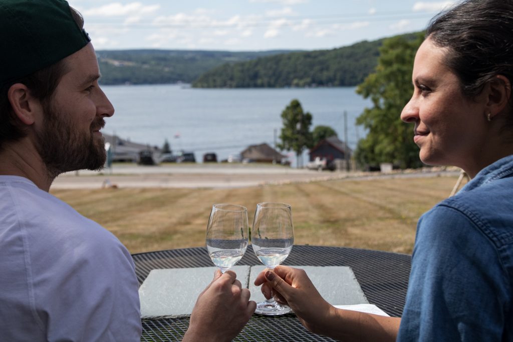 A man and woman cheers while wine tasting at Ravines Wine Cellars overlooking Keuka Lake in the Finger Lakes region of upstate New York.