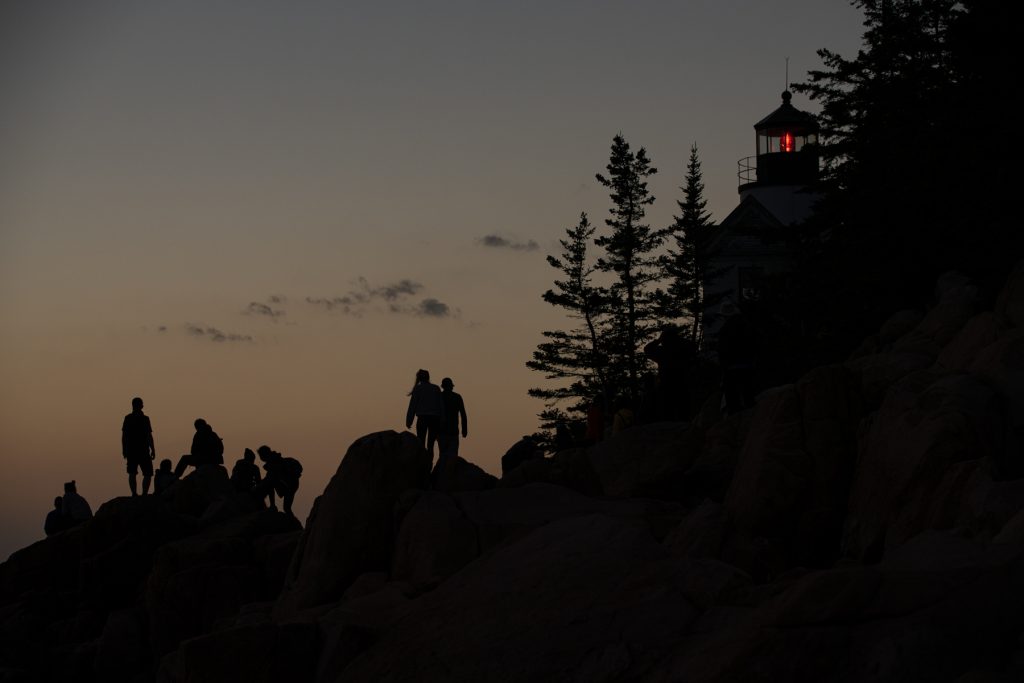 Silhouettes of people viewing the sunset at Bass Harbor Head Lighthouse at Acadia National Park in Maine.