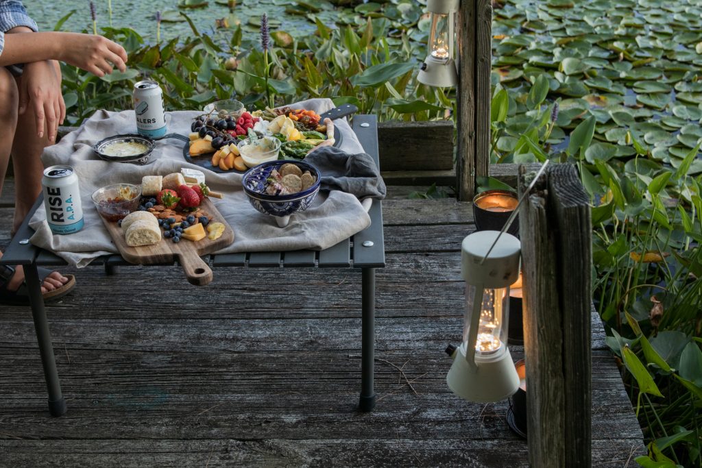 Table in a bag from Crate & Barrel on a deck overlooking a Lilly pond. On the table are cheese and charcuterie boards and beer.