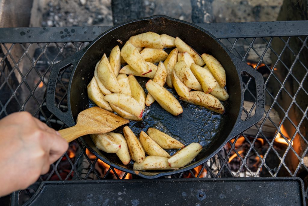 A Lodge Cast Iron double-handle pan with cinnamon apples being cooked over the campfire. 