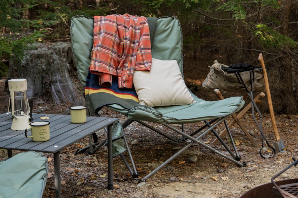 LL Bean's classic plaid flannel thrown on top of a Canada Woods Mammoth chair that's sitting near a campfire.