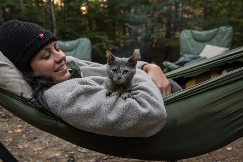 A woman wearing a New Balance beanie hat and holding her cat in a hammock.