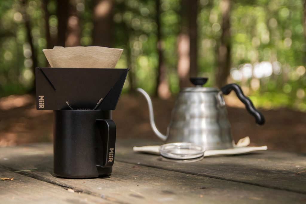 MiiR Pourigami on top of a MiiR mug with a tea kettle in the background. An image of making coffee at the campsite.