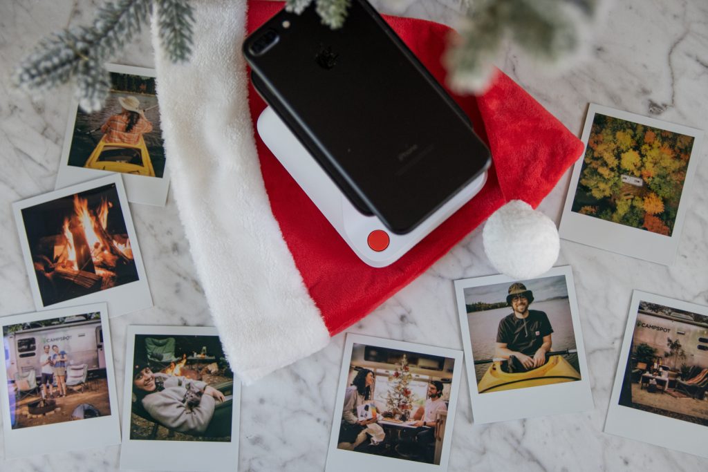 A phone atop the Polaroid Lab Instant Printer and Santa hat with Polaroid image of camping beneath. 