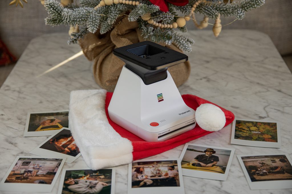 Polaroid Lab Instant Printer sitting atop a Santa hat, underneath a Christmas tree and surrounded by polaroid photos.