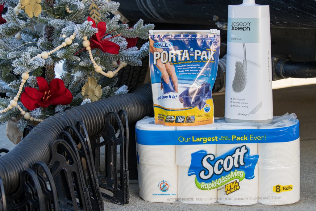 Scott RV toilet paper, Porta Pak Holding Tank Deodorizer Drop-Ins, and a Camco sewage hose and hose support next to a Christmas tree.