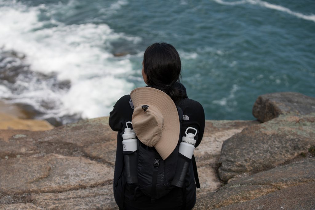 Woman overlooking the seacoast in Acadia National Park with two Takeya water bottles in her backpack.