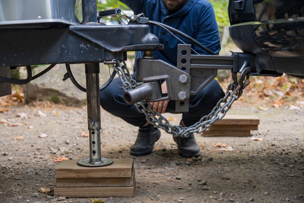 A man lowers his trailer onto a wooden jack pad.