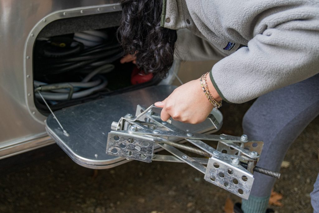 A woman takes out tire chocks from a storage compartment. 