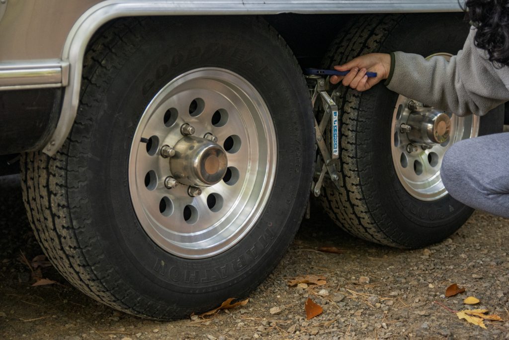 A woman uses a wrench to tighten the tire chocks between the wheels of an RV.