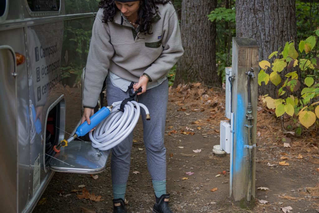 A woman takes out a water house and filter to connect her RV to a city water connection.