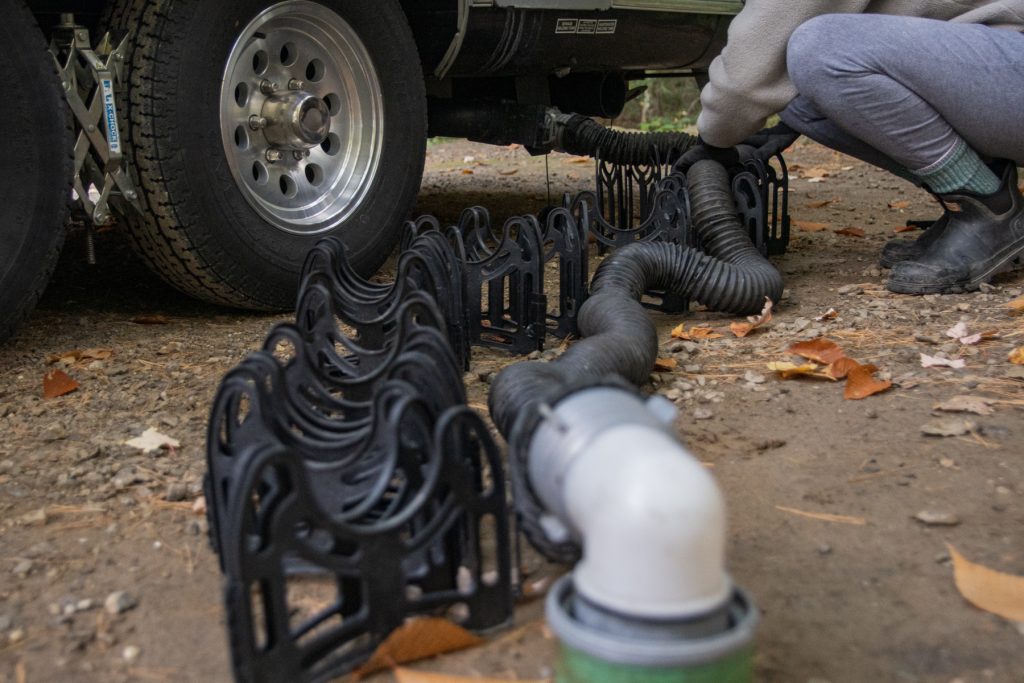 A woman positions her RV sewage hose onto a sewage hose support.