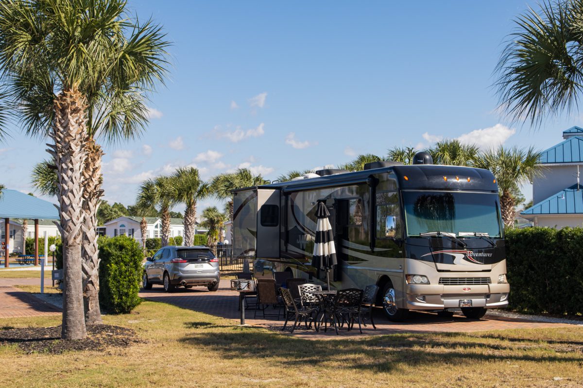 A Class A motorhome coach sits at a campsite at Emerald Coast RV Resort in Panama City Beach, Florida. The RV is surrounded by palm trees.