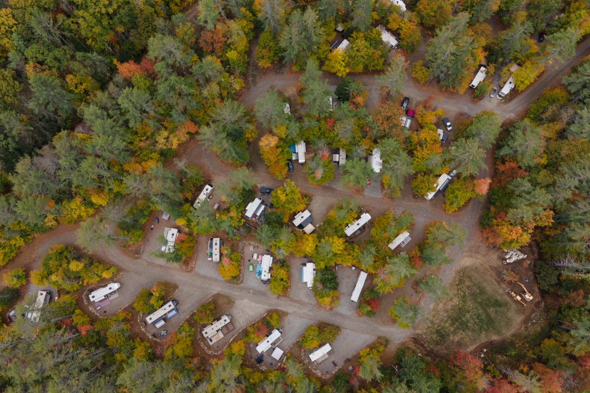 An aerial view of Ames Brook Campground in Ashland, New Hampshire with RV's spaced out and sitting in their campsites. The fall foliage can be viewed with bright colors poking out.