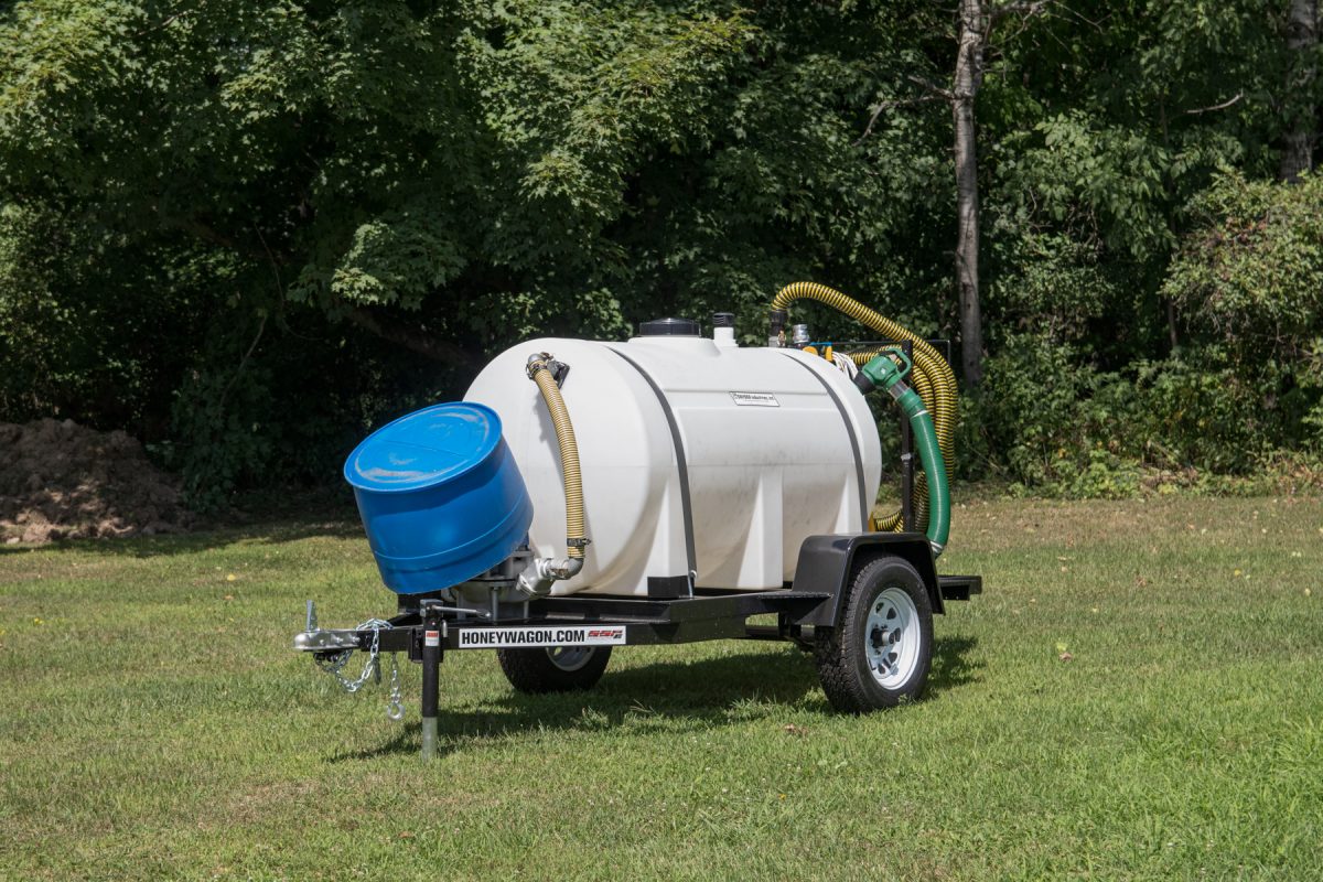 A honey wagon trailer sits in a grassy field at a campground. Honey wagons travel around the campground and pump out RV black and grey water tanks.