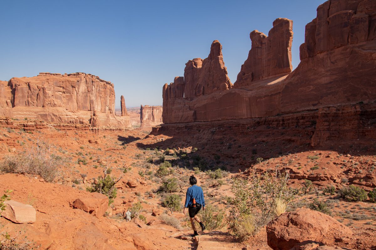 A woman hikes along the Park Avenue Trail in Arches National Park in Moab, Utah. The Courthouse Towers can be seen at the end of the trail. 