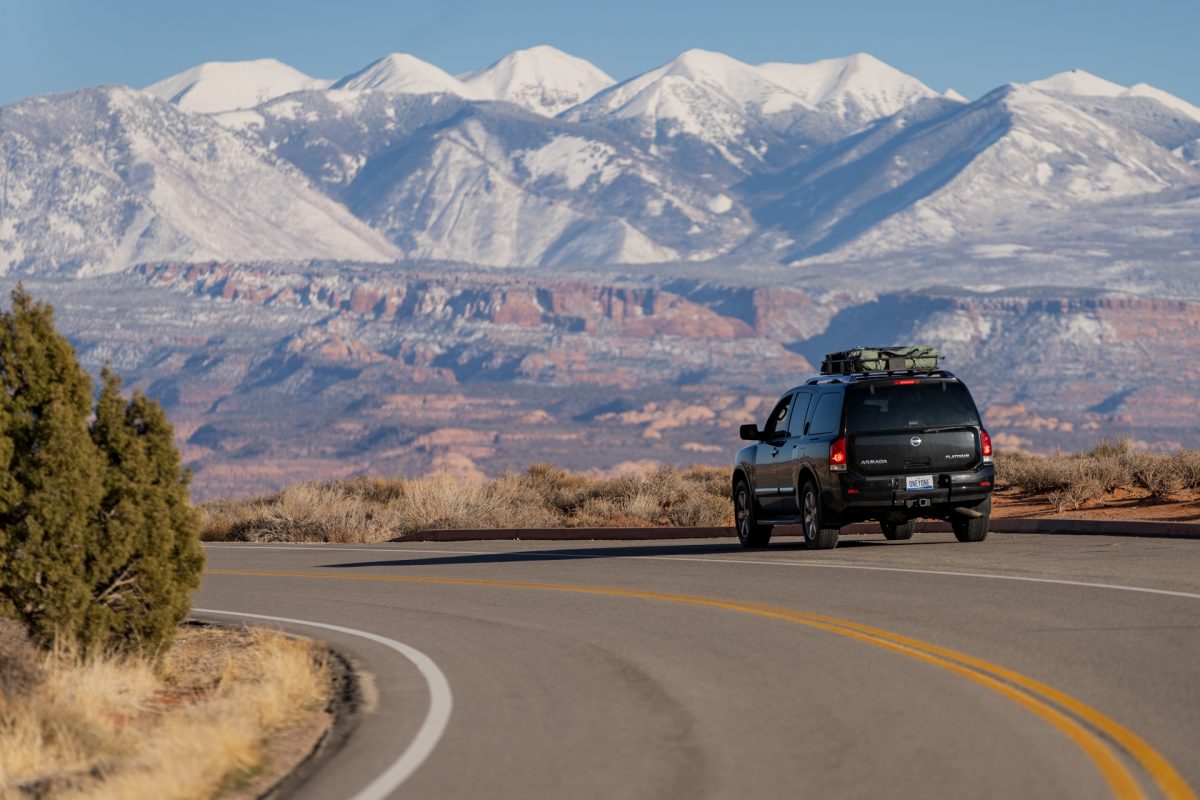 A black SUV is parked on a pull out that looks toward the La Sal Mountains. The mountains are covered in white snow.