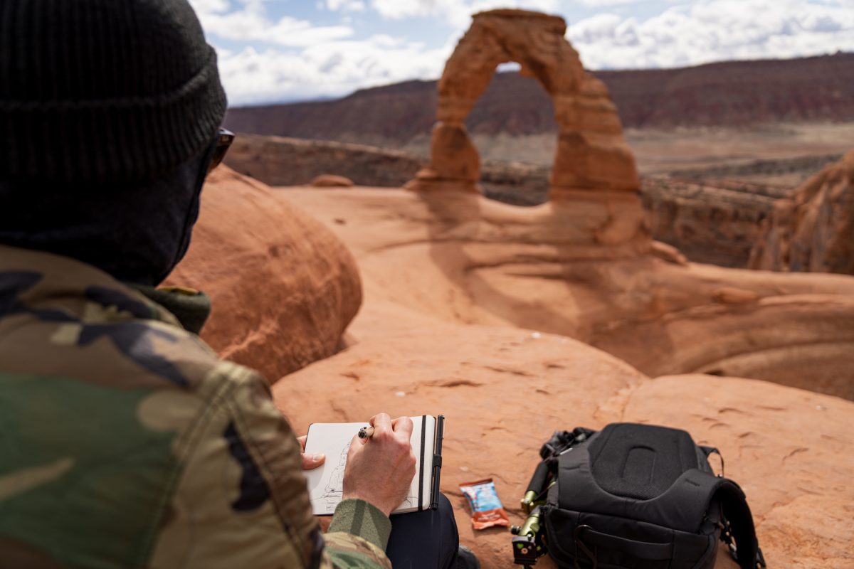 A man draws Delicate Arch with Delicate Arch seen in the background at Arches National Park in Moab, Utah.