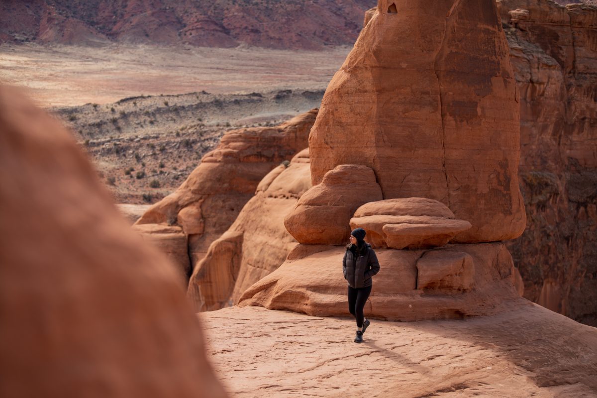 A woman looks out to the desert while standing underneath Delicate Arch in Arches National Park located in Moab, Utah.