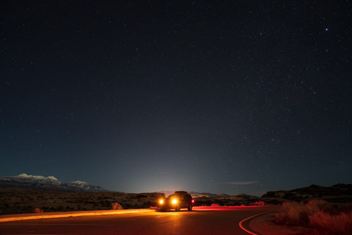 In the night, an SUV shines its lights while parked at the Balanced Rock pull out in Arches National Park in Moab, Utah.