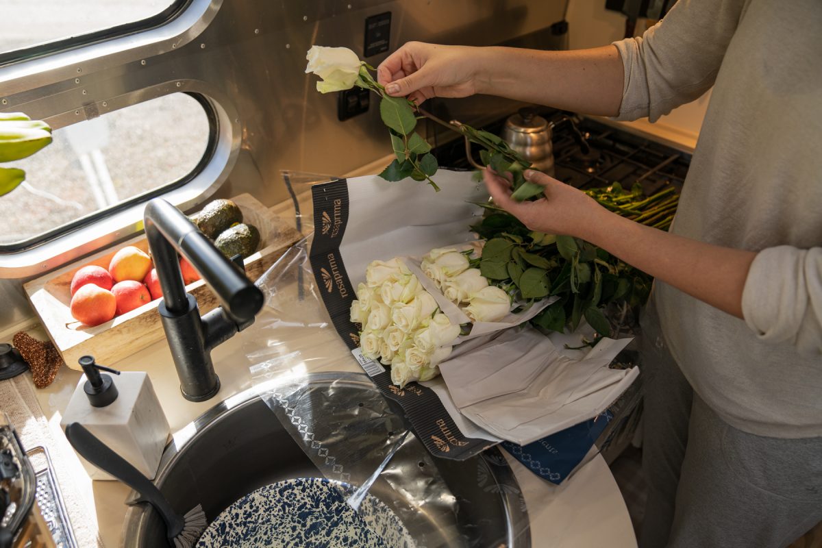 After opening up a packaged bouquet of white roses, a woman de-stems the roses inside an Airstream trailer.