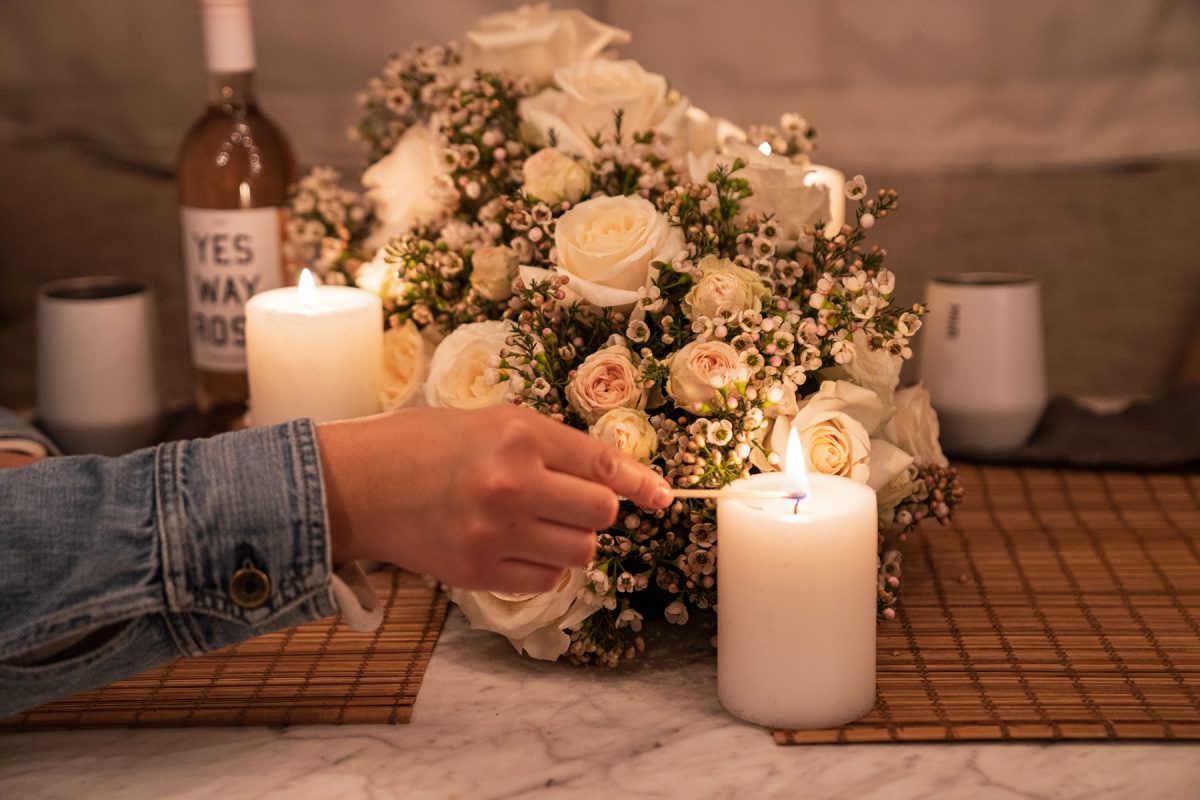 A person lights a candle that is sitting on top of an Airstream RV table and next to a floral arrangement of roses and wax flowers.