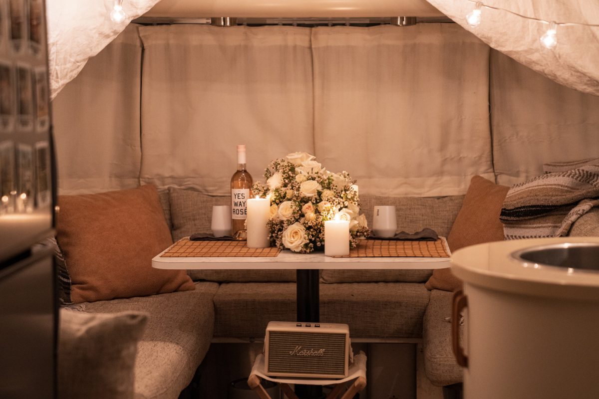 The view of a dinette area of an RV Airstream trailer decorated by Valentine's day flowers, cafe lights, and linen tarps. 