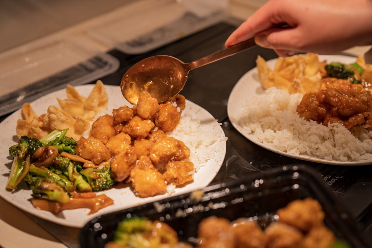 A person serves Chinese takeout onto plates. 