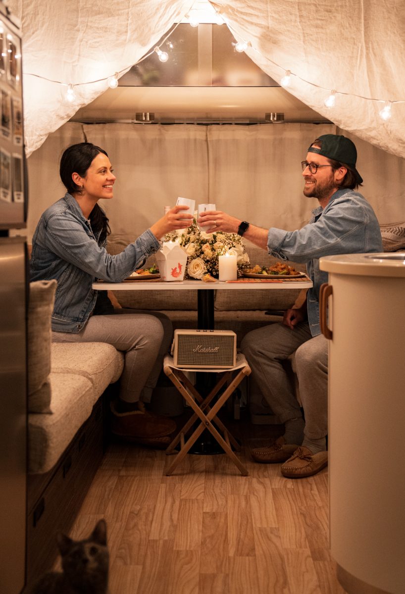 A woman and a man cheers while enjoying a Valentine's date night inside of their Airstream RV trailer.