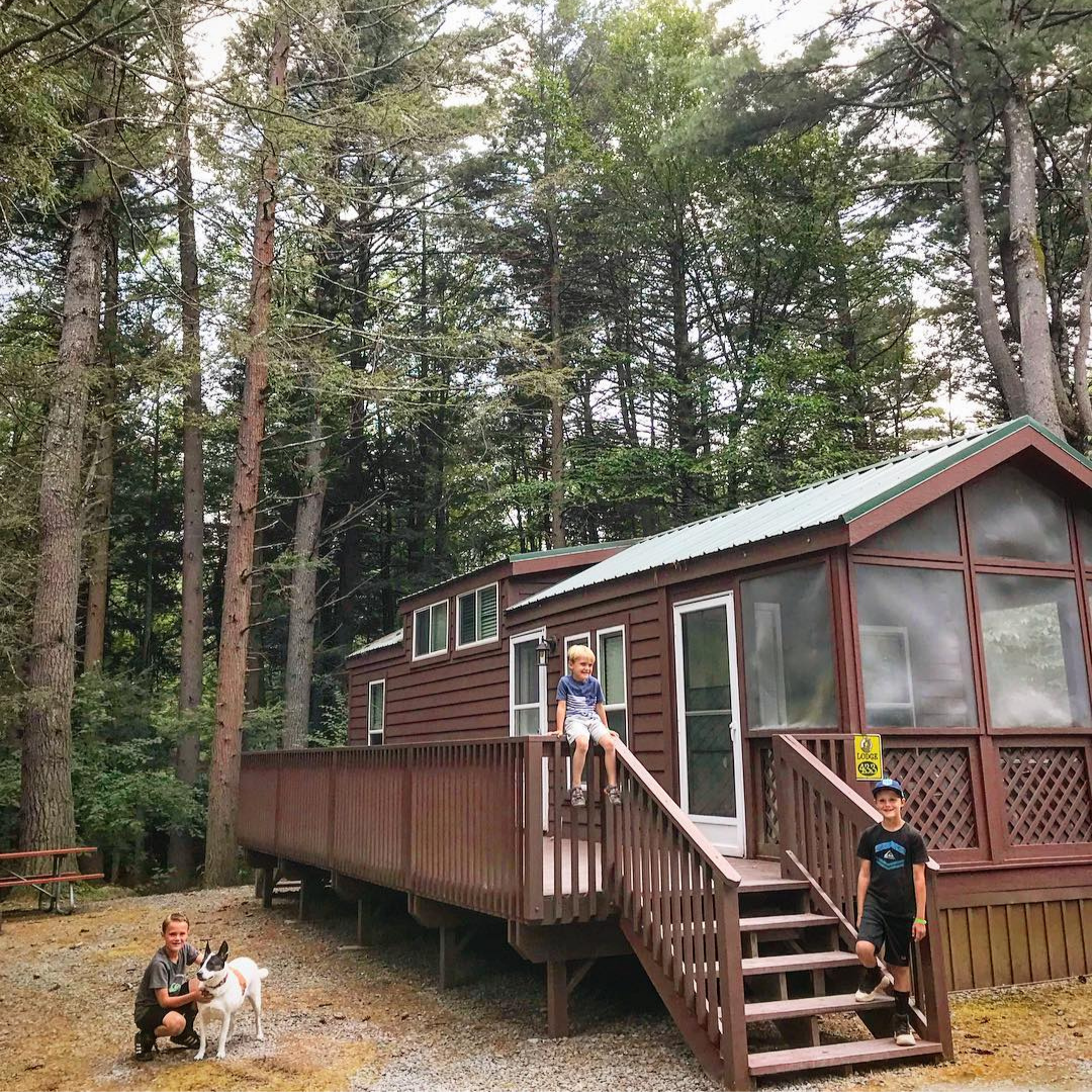 Three boys playing outside of a cabin with forest in back. 